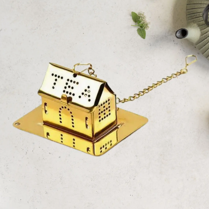 Gold tea infuser shaped like a house on a light surface