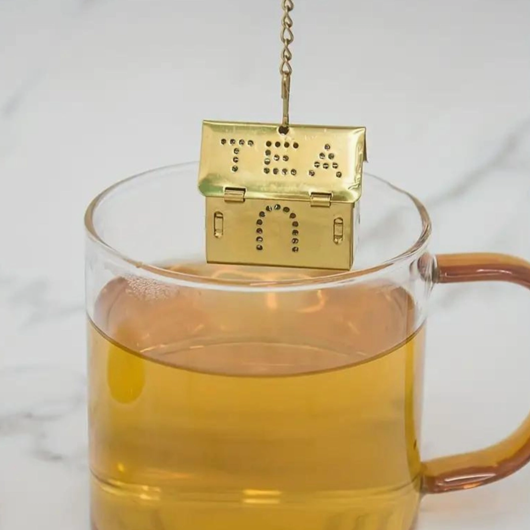 Gold tea infuser in a glass of tea on a marble surface